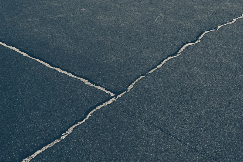 A close view of cracks running across a dark asphalt court surface — tennis court resurfacing, Adelaide. Illustrative example.